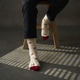 Person wearing socks with horse pattern and red toes, sitting on a wooden stool.